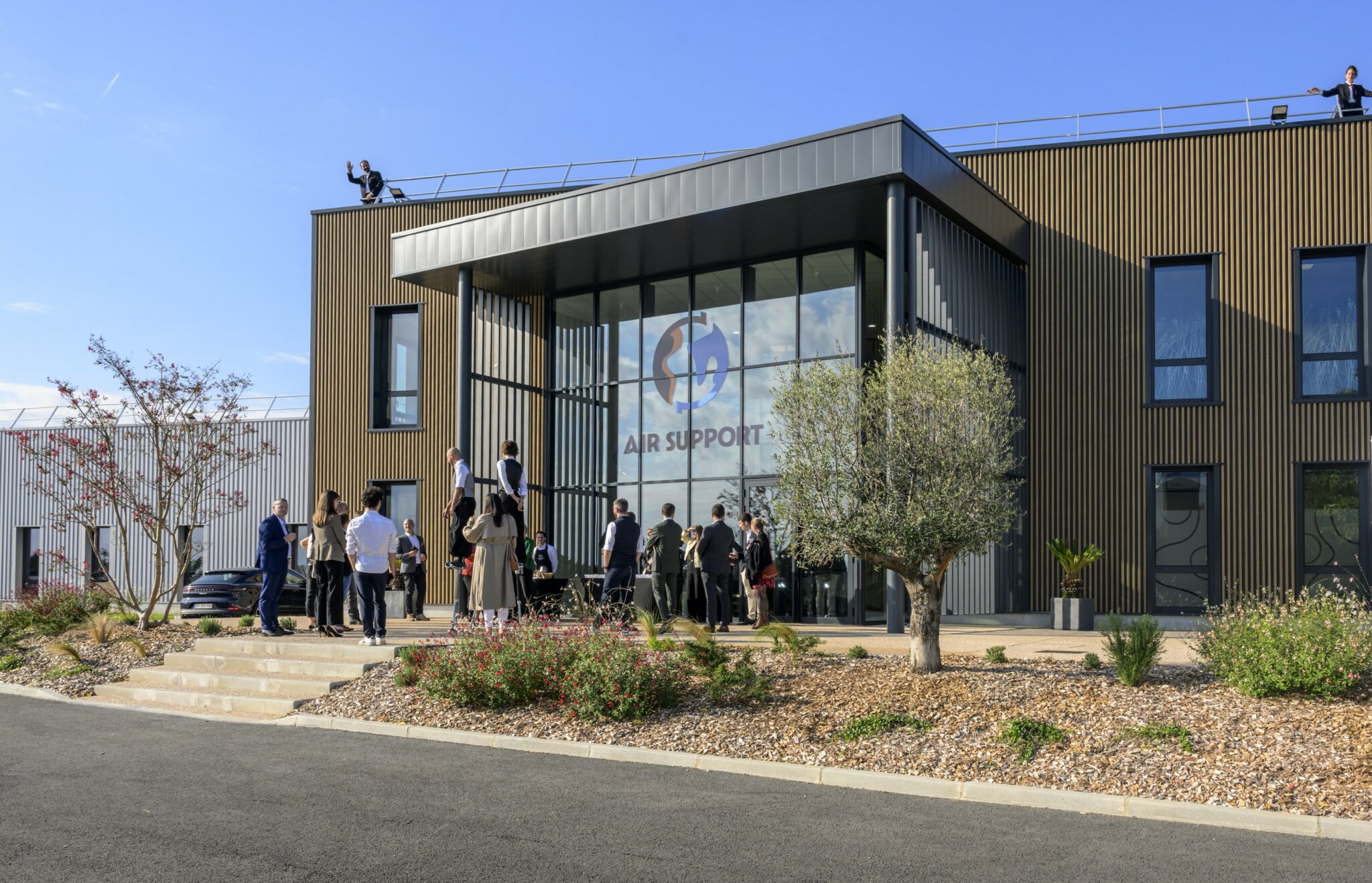 Inauguration des nouveaux locaux d'Air Support à Pujaudran : rassemblement des équipes devant le bâtiment moderne de l'entreprise aéronautique lors de l'événement.